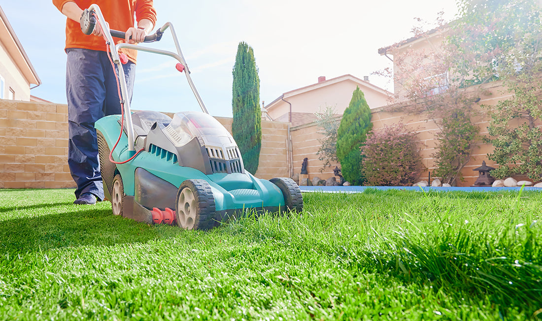 Man wearing a red shirt and jeans mowing his lawn