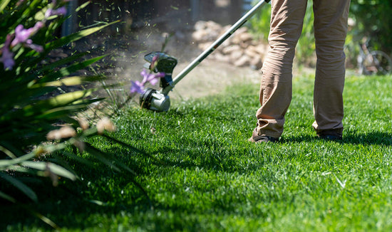 Person in khaki pants edging a green lawn