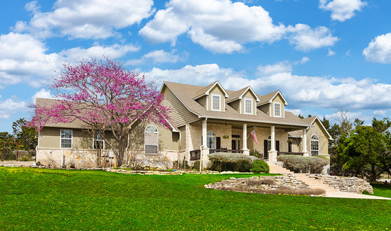 Beautiful cream-colored house with a bright green front lawn and cherry blossom tree on a sunny day